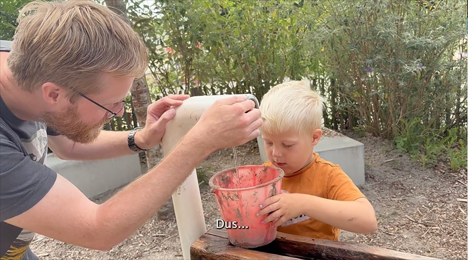 Pedagogisch professional Dirk-Jan helpt kind bij waterput met vullen emmer