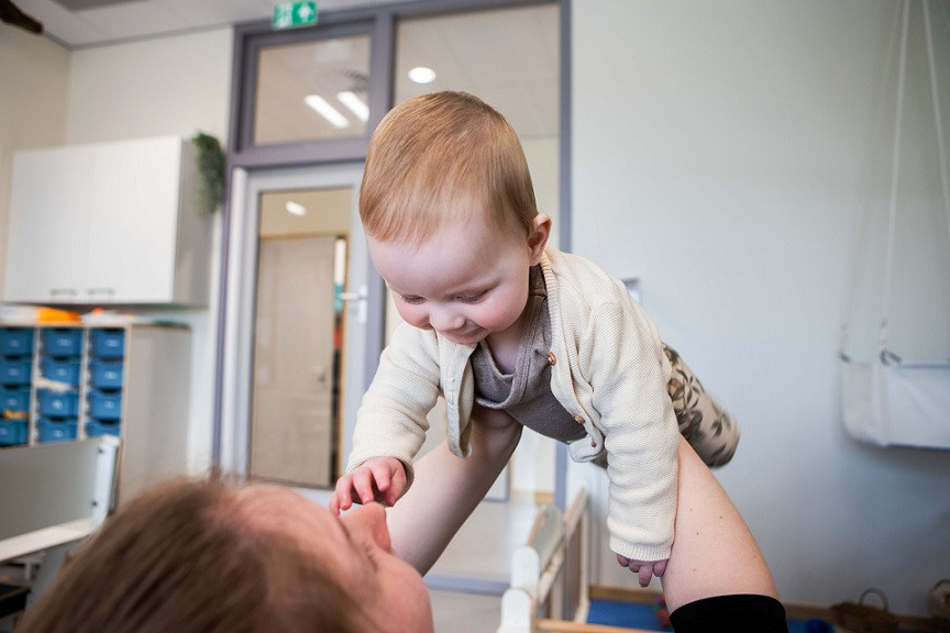 Pedagogisch medewerker houdt baby in de lucht