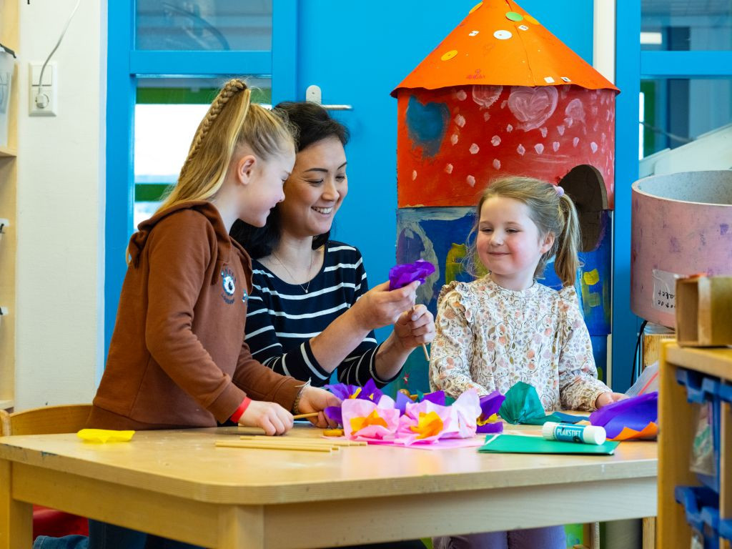 pedagogisch medewerker en twee kinderen maken papieren bloemen