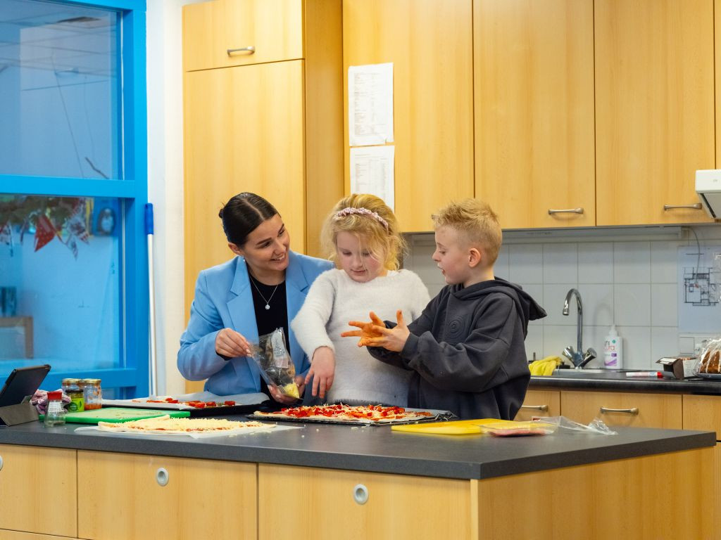 twee kinderen en pedagogisch medewerker maken zelf pizza