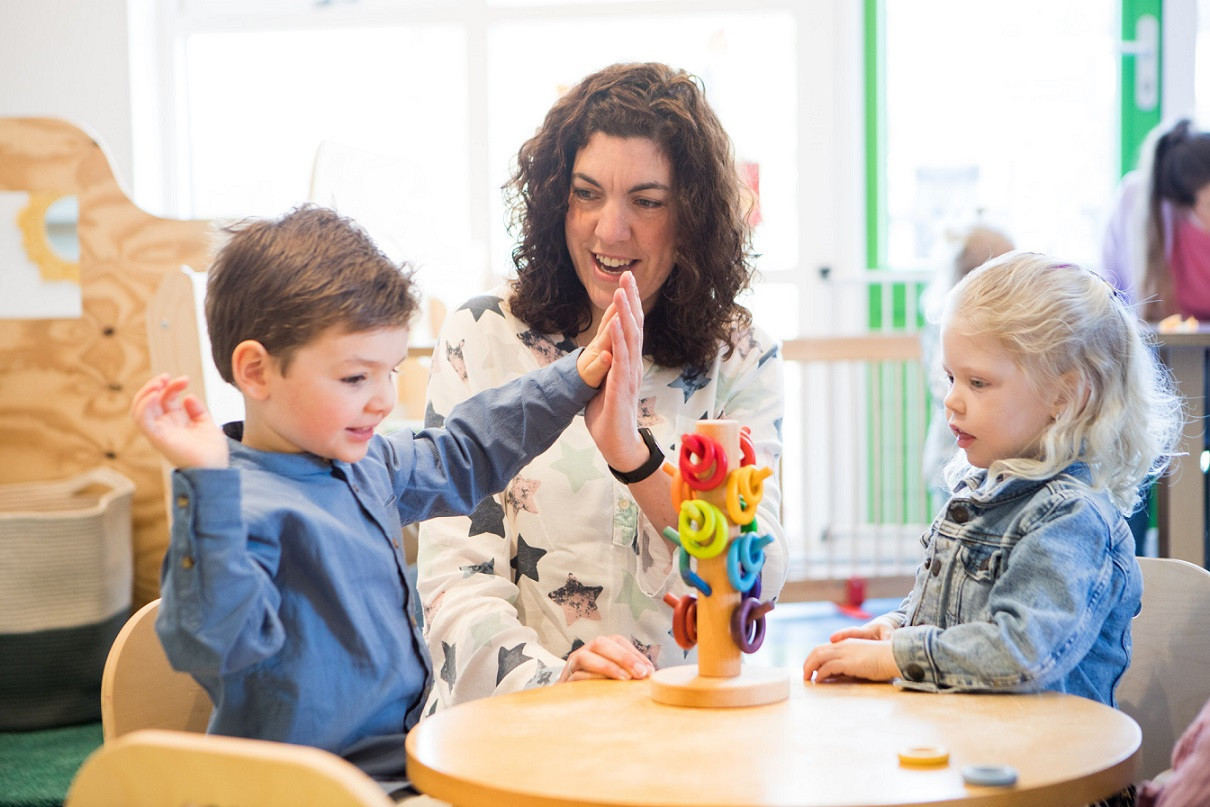 Pedagogisch medewerker geeft high five aan peuter
