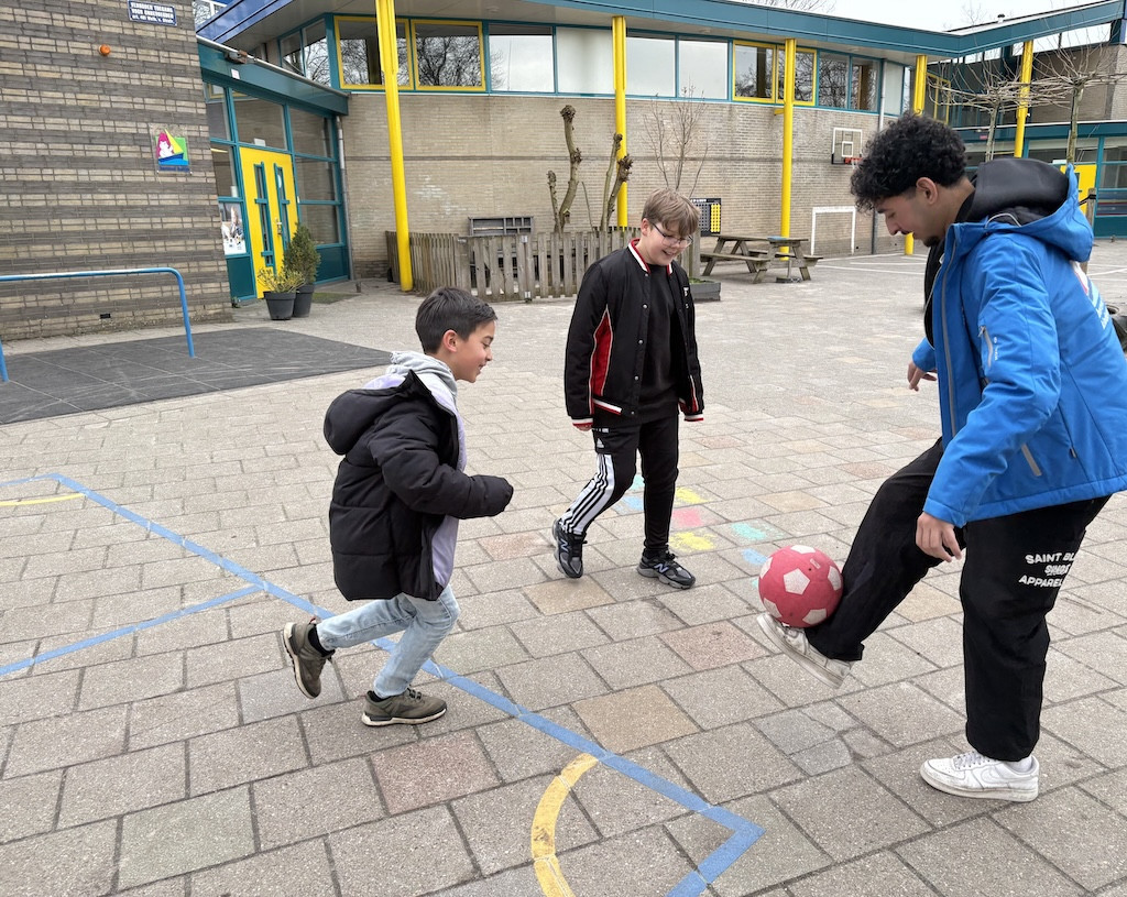 Pedagogisch professional Ayoub speelt voetbal met jongens van BSO De Kersenboogerd