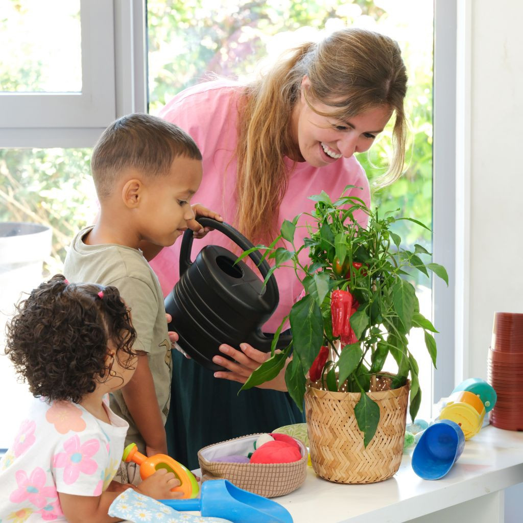 pedagogisch professional en kind geven samen binnen een paprikaplant water