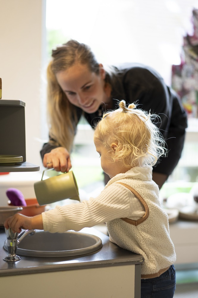 Pedagogisch medewerker en kind samen in de keuken