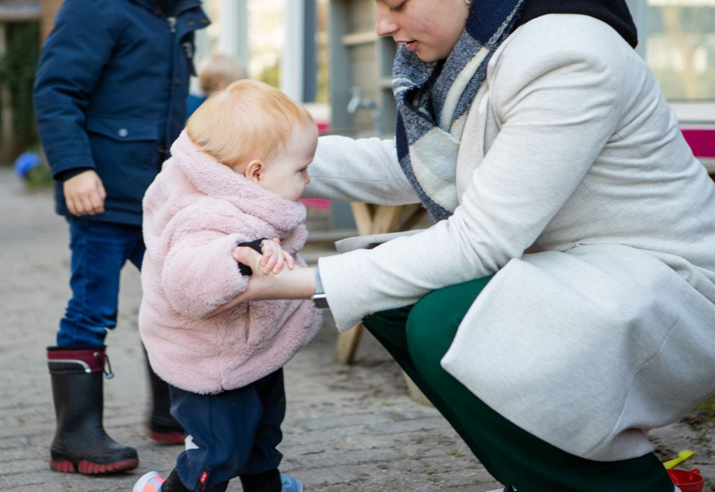 pedagogisch professional helpt klein kind met lopen