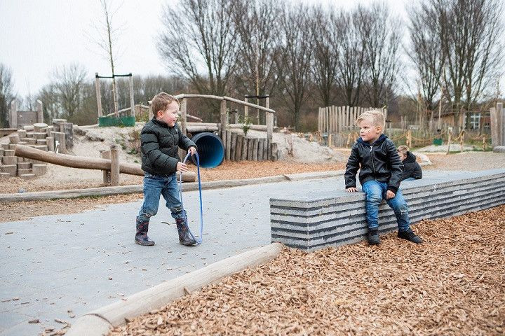 een kind met hoepel vast en een kind dat op stenen rand zit