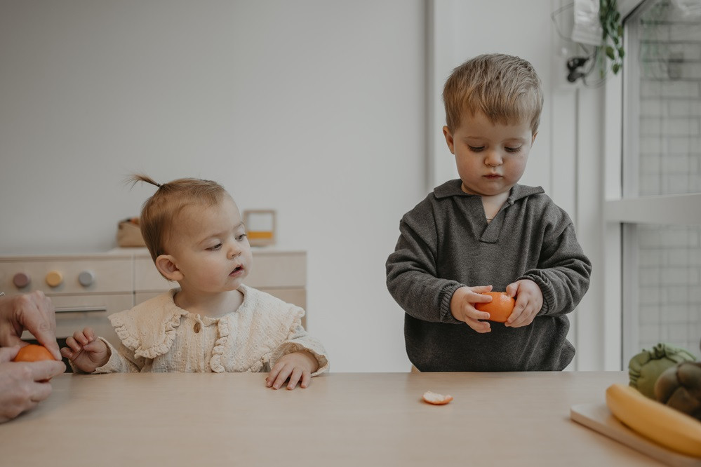 jongetje pelt een mandarijn en meisje kijkt toe