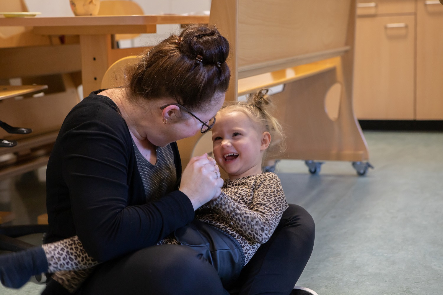 pedagogisch professional zit op grond en heeft kind op schoot dat lacht