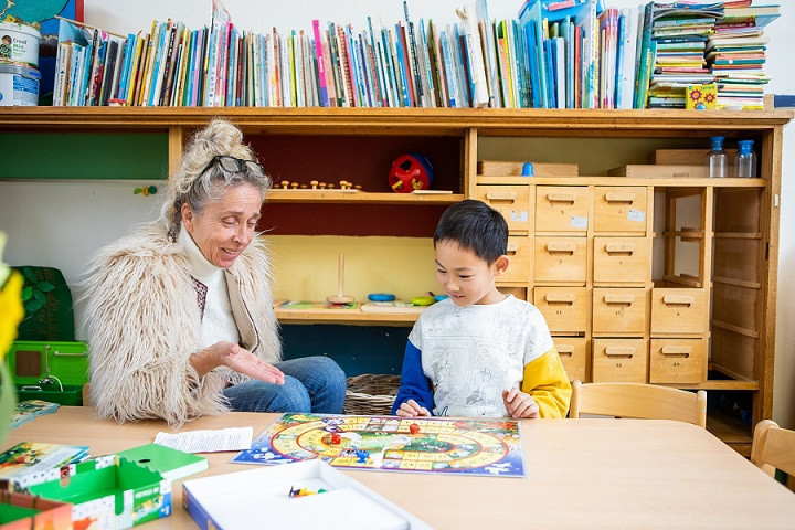 pedagogisch professional en kind spelen ganzenbord aan tafel