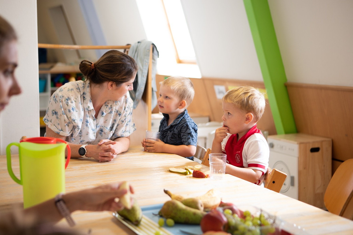 kinderen zitten met pedagogisch professional fruit te eten aan tafel