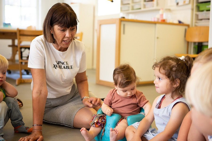 kinderen zitten met pedagogisch professional op grond in kring