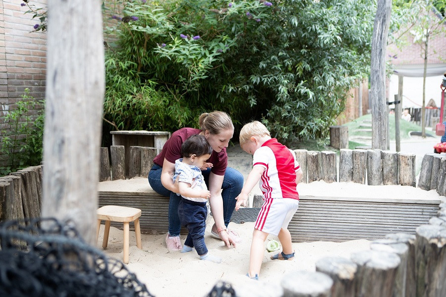 twee kinderen en pedagogisch professional spelen samen in het zand