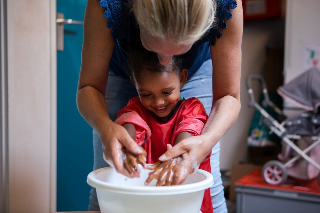 pedagogisch professional helpt kind met handen wassen in teiltje