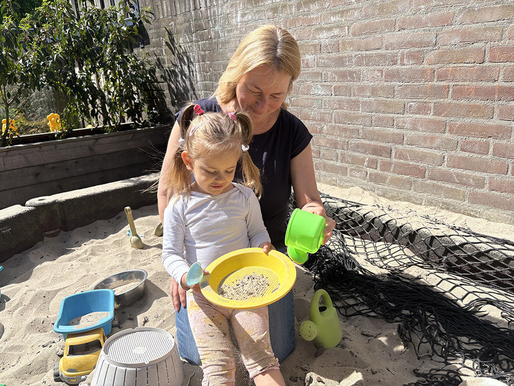 Pedagogisch professional Annemieke speelt met een peuter in de zandbak