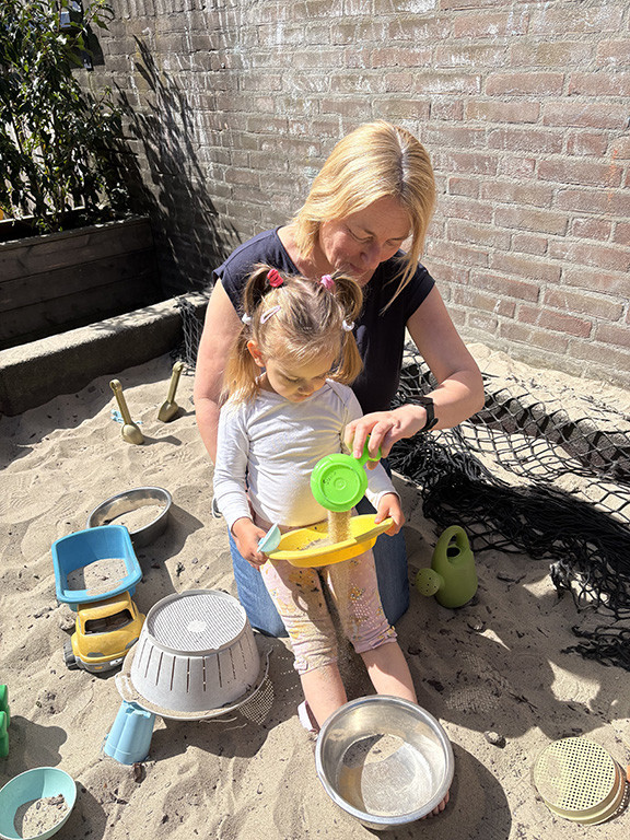 Pedagogisch professional speelt met een peuter in de zandbak