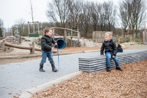 een kind met hoepel vast en een kind dat op stenen rand zit