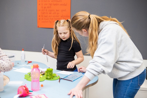 Meisje vertelt wat zij knutselt aan pedagogisch professional