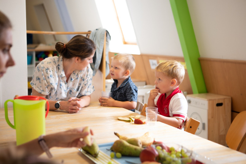 kinderen zitten met pedagogisch professional fruit te eten aan tafel