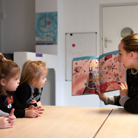 Pedagogisch medewerker leest peuters voor aan tafel